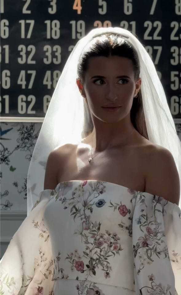 Bride in floral dress standing in soft light with a backdrop of numbers.
