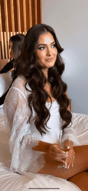Woman in lace nightwear holding a glass of champagne, sitting on a bed.