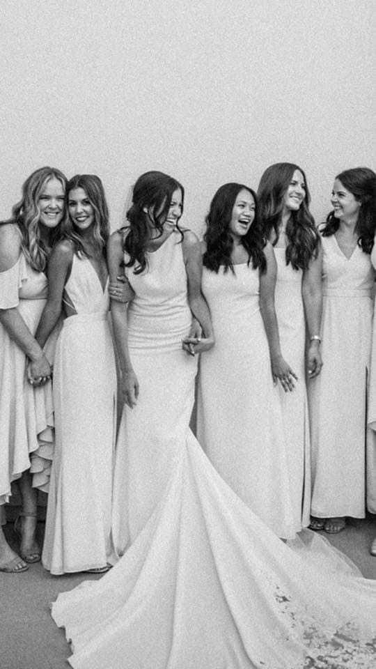 Bride and bridesmaids in elegant dresses, laughing and enjoying a joyful moment together.